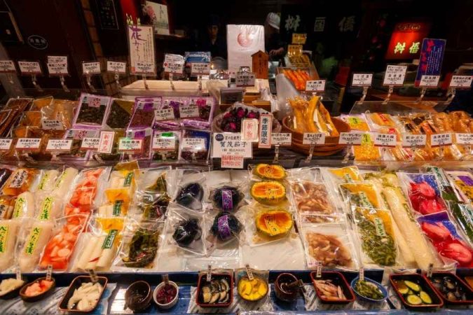 Étal coloré d'un marché gastronomique japonais proposant une large variété de légumes marinés et de spécialités locales emballées.