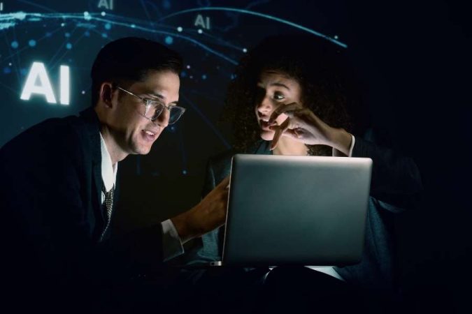 Un homme et une femme d'affaires en costume analysent ensemble des données sur un ordinateur portable dans l'obscurité, devant des graphiques d'IA lumineux.