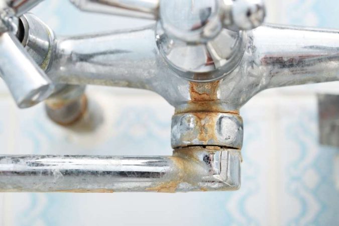Un robinet de salle de bain chromé présentant d'importantes traces de calcaire incrustées au niveau des joints.