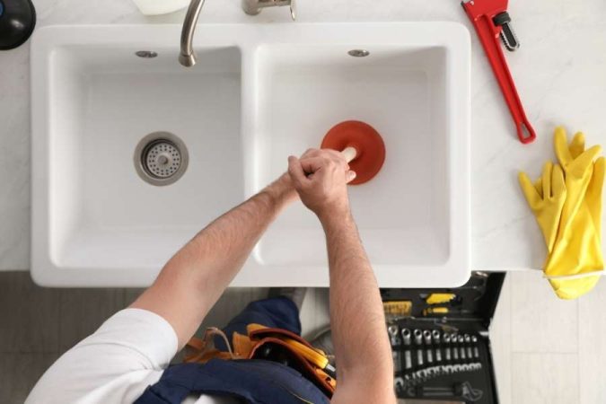 Un plombier utilise une ventouse pour déboucher une canalisation de lavabo dans une cuisine moderne.