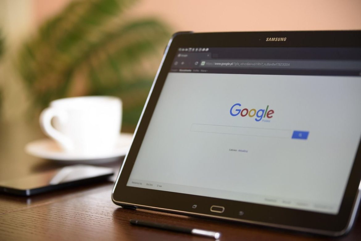 Une tablette Samsung est posée sur une table en bois. Son écran affiche la page d'accueil de Google, avec la barre de recherche centrale et le logo coloré. En arrière-plan, une tasse de café blanche floue et un smartphone sont visibles. Cette image illustre parfaitement pourquoi la création d’un site internet est devenue incontournable pour être visible sur les moteurs de recherche comme Google.